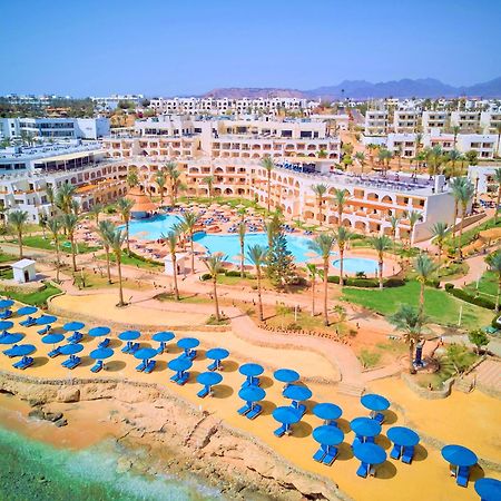 Pickalbatros Royal Grand Sharm - Adults Friendly 16 Years Plus ภายนอก รูปภาพ The photo shows a vibrant resort area with several buildings that appear to be accommodations or hotel units. There are multiple swimming pools surrounded by palm trees, creating a tropical atmosphere. In the foreground, there is a beach area with sa
