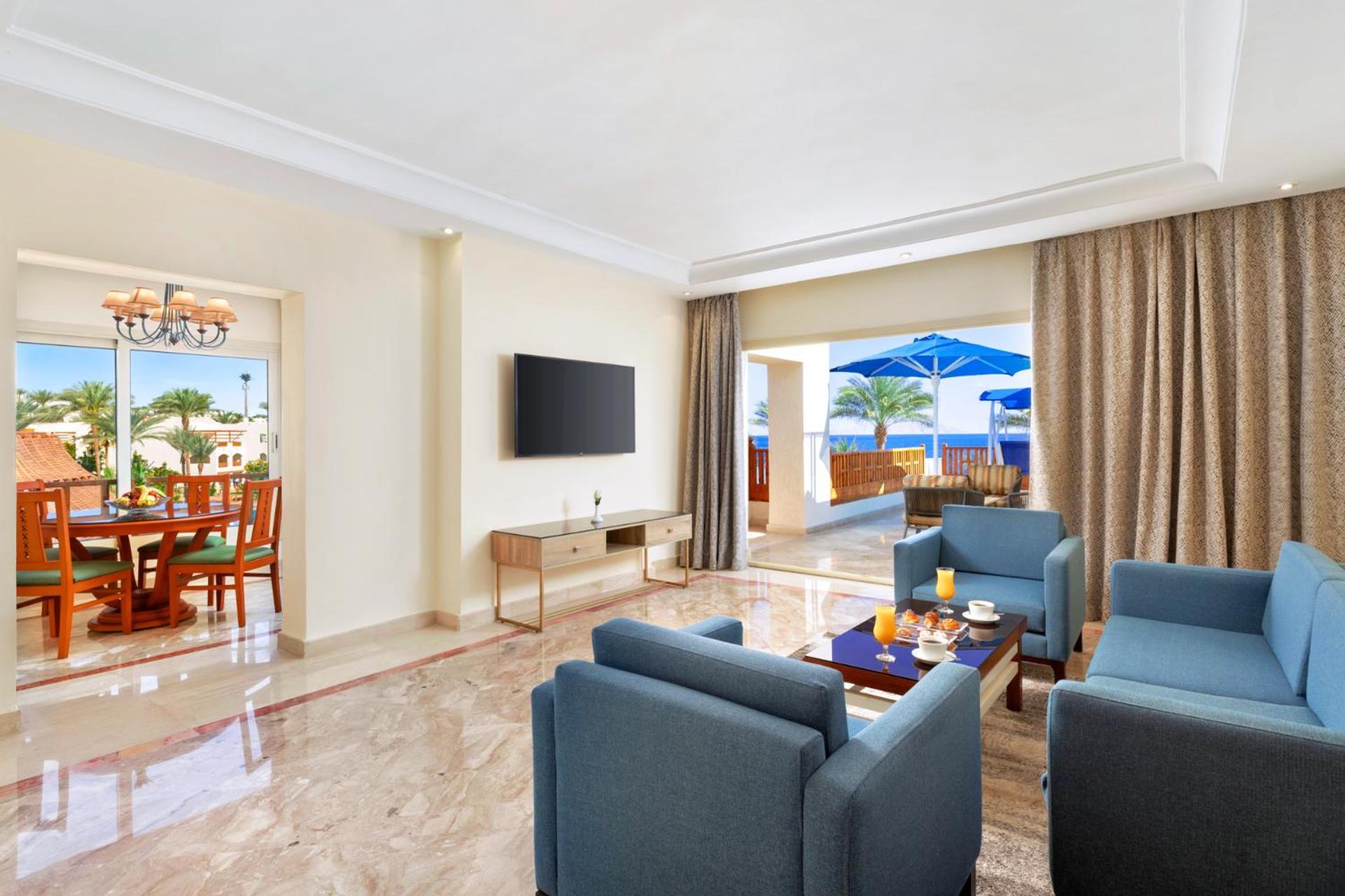 Pickalbatros Royal Grand Sharm - Adults Friendly 16 Years Plus ภายนอก รูปภาพ The photo shows a modern and spacious living area. There are several blue chairs arranged around a coffee table, which holds some refreshments. A large flat-screen TV is mounted on the wall, and there are sliding glass doors that open to an outdoor a