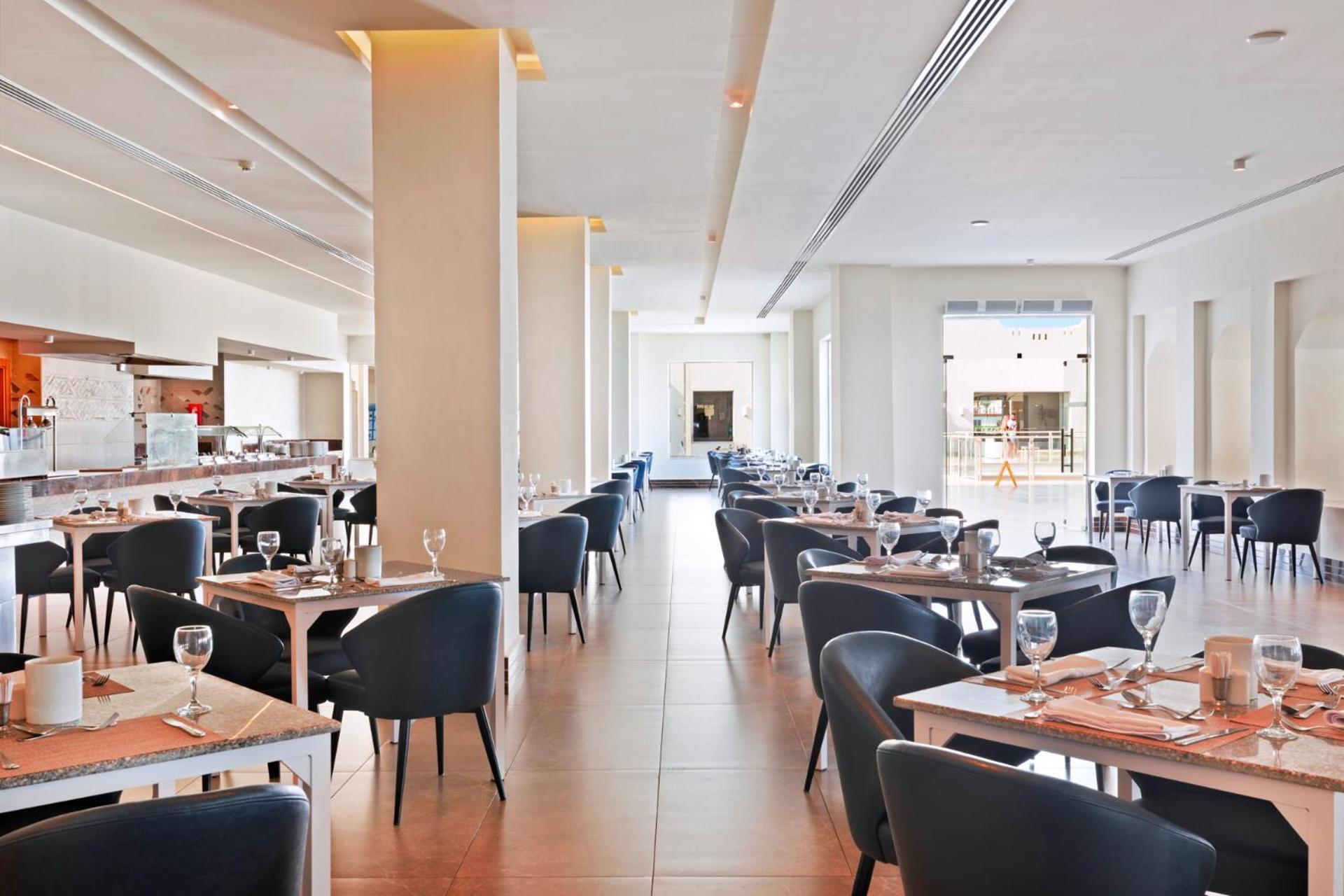 Pickalbatros Royal Grand Sharm - Adults Friendly 16 Years Plus ภายนอก รูปภาพ The photo shows the interior of a modern restaurant. The space is bright and airy, featuring large windows that allow natural light to flood in. There are several tables arranged throughout the room, each covered with placemats and set with glasses a