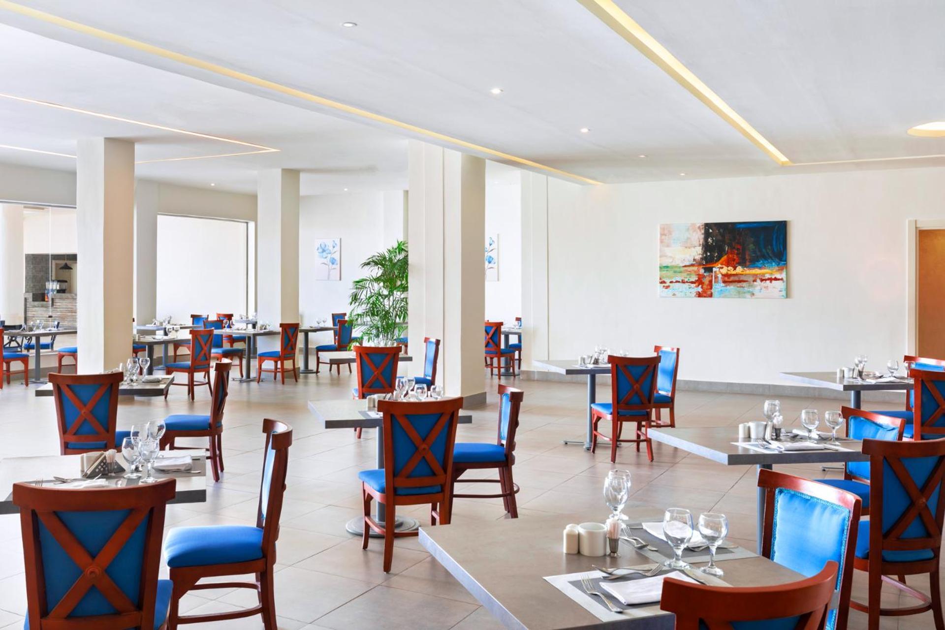Pickalbatros Royal Grand Sharm - Adults Friendly 16 Years Plus ภายนอก รูปภาพ The photo shows an interior of a restaurant featuring a modern and spacious design. The floors are tiled, and the walls are painted in neutral tones. The seating consists of wooden chairs with blue cushions arranged around tables, which are set with 