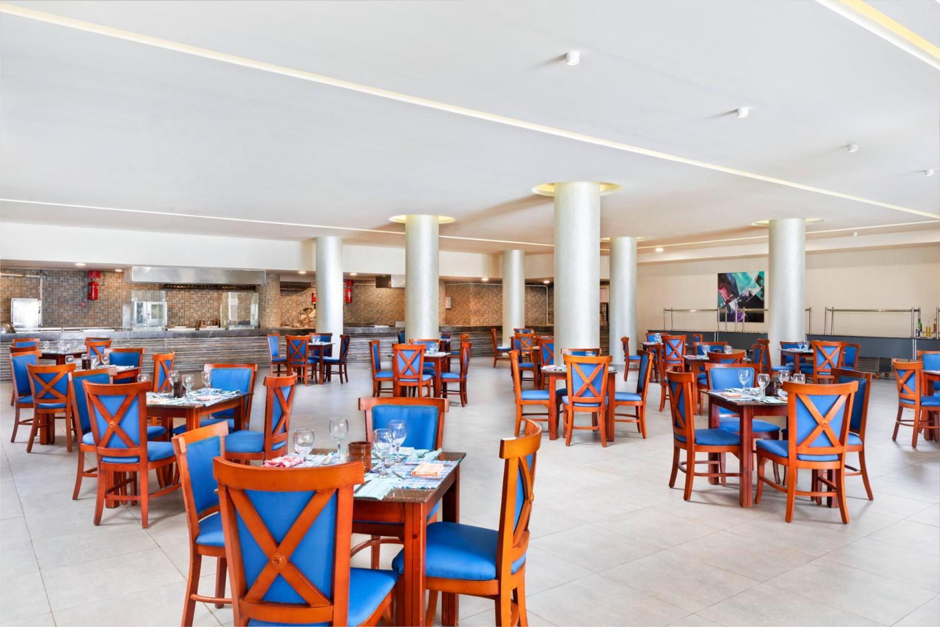 Pickalbatros Royal Grand Sharm - Adults Friendly 16 Years Plus ภายนอก รูปภาพ The photo depicts a spacious dining area in a restaurant. The room features several wooden tables, each with blue chairs. The chairs have a unique design with prominent X-shaped backs. The flooring is light-colored tile, and the walls are painted in 