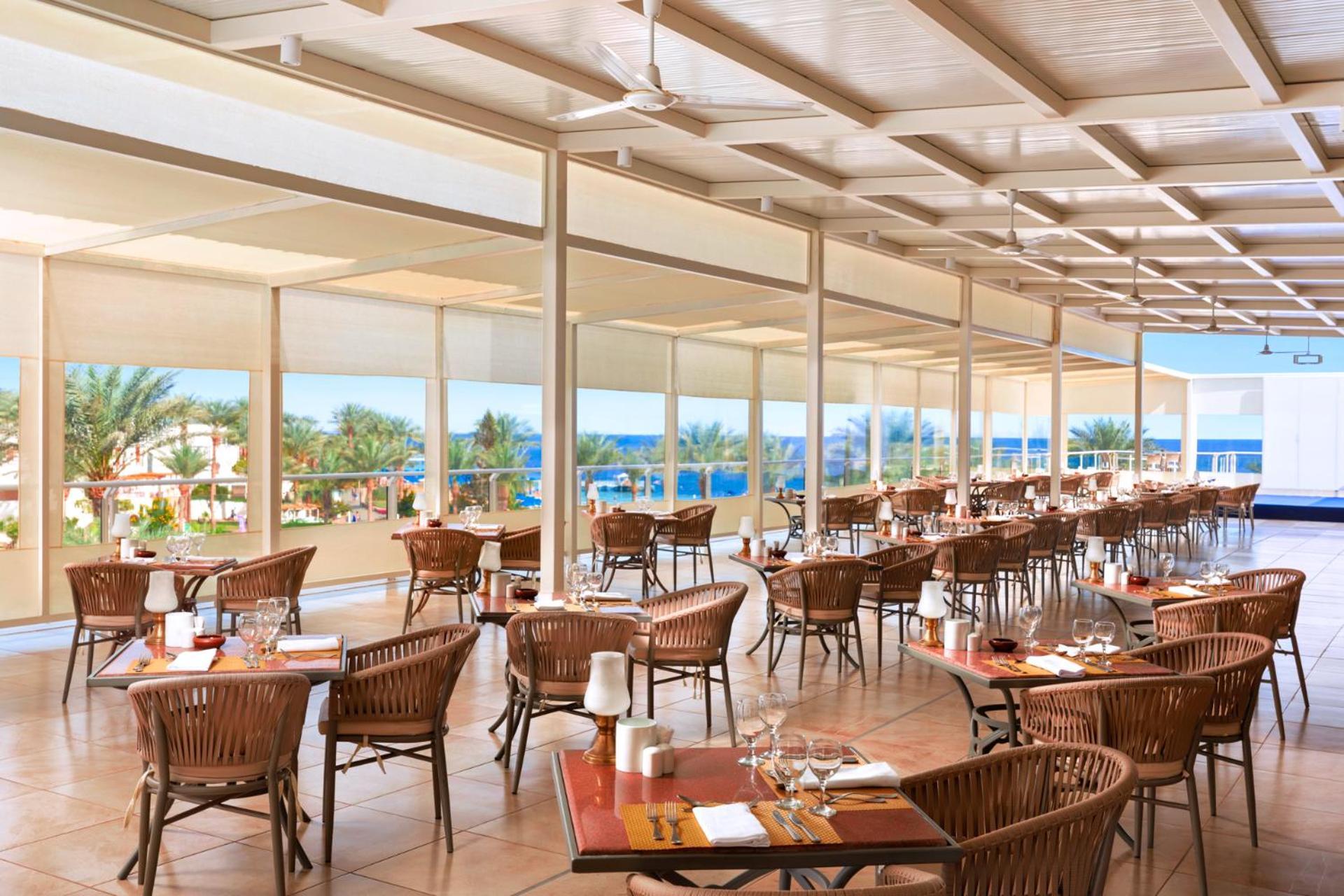 Pickalbatros Royal Grand Sharm - Adults Friendly 16 Years Plus ภายนอก รูปภาพ The photo shows a spacious dining area in a restaurant with a modern and airy design. It features numerous wooden tables set with glasses and cutlery, arranged in a way that gives an open feel. Large windows provide a view of the outside, showcasing 
