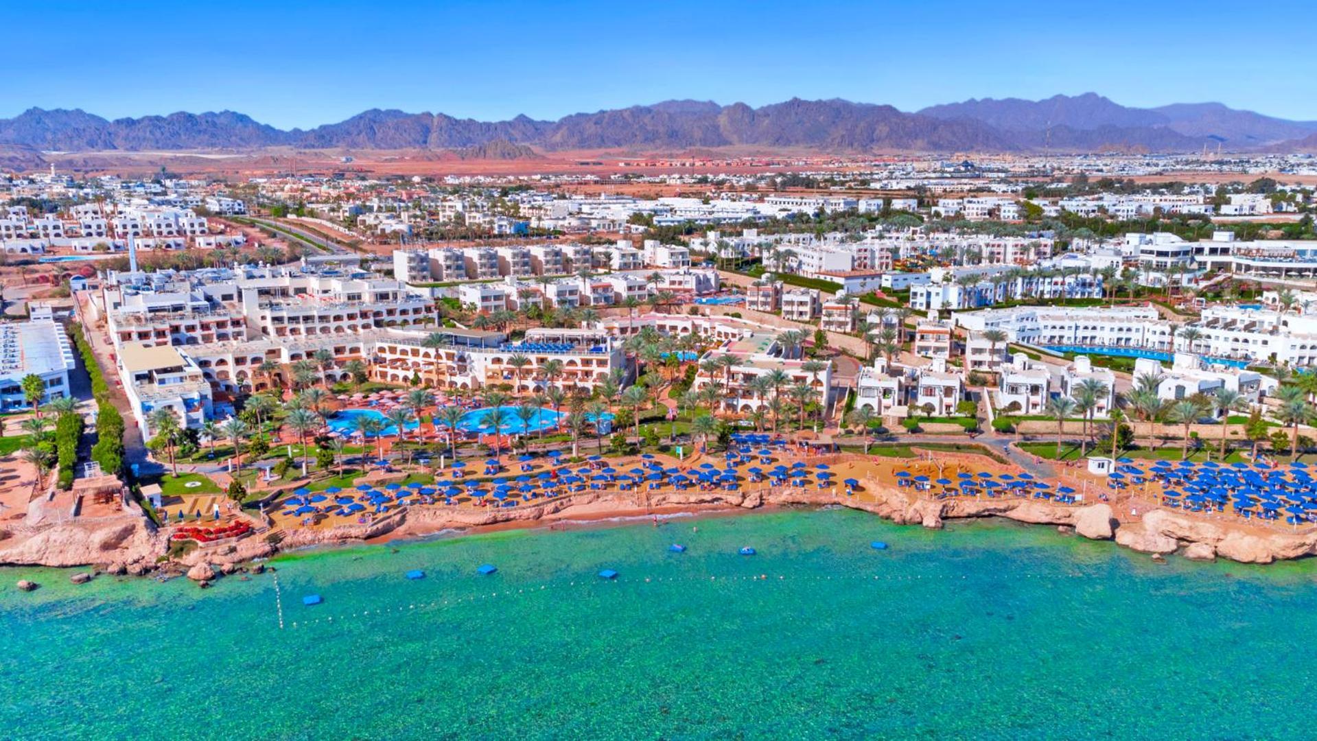 Pickalbatros Royal Grand Sharm - Adults Friendly 16 Years Plus ภายนอก รูปภาพ The photo shows an aerial view of a resort located by the coast. There are several swimming pools surrounded by sun loungers and umbrellas, as well as a beach area with clear turquoise water. In the background, there are multiple buildings of the res