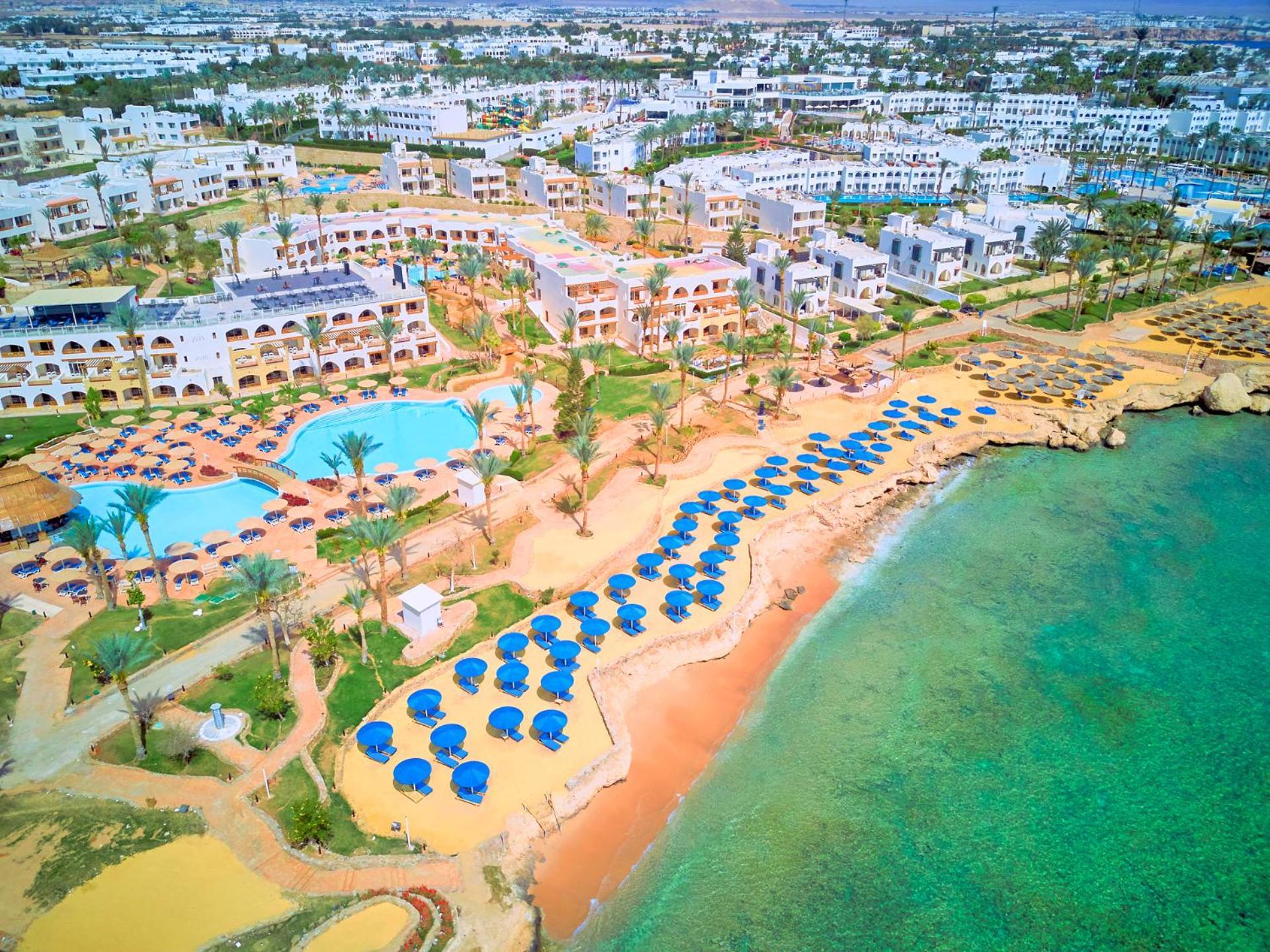 Pickalbatros Royal Grand Sharm - Adults Friendly 16 Years Plus ภายนอก รูปภาพ The image shows an aerial view of a resort area by the beach. There is a swimming pool in the center, surrounded by palm trees and sun loungers. The sandy beach features numerous umbrellas arranged in rows for shade. In the background, there are seve
