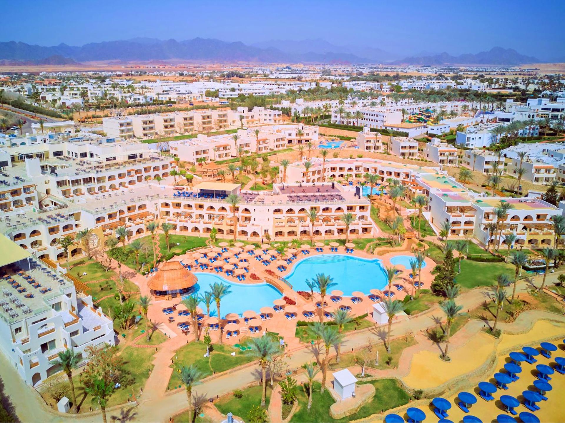 Pickalbatros Royal Grand Sharm - Adults Friendly 16 Years Plus ภายนอก รูปภาพ The photo shows an aerial view of a resort complex. There are several buildings arranged around a central area that features swimming pools. The pools are surrounded by palm trees and lounge chairs, indicating a tropical or sunny climate. In the back