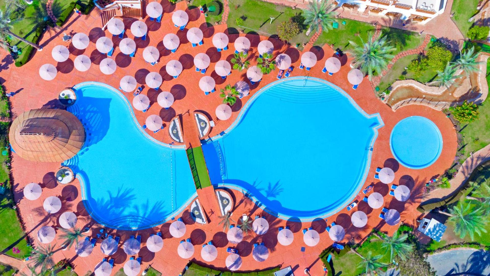 Pickalbatros Royal Grand Sharm - Adults Friendly 16 Years Plus ภายนอก รูปภาพ The photo shows an aerial view of a large swimming pool area, shaped in a distinctive layout resembling two interconnected pools. Surrounding the main pool are numerous umbrellas, providing shade for visitors. The pool area is set on a reddish-colore
