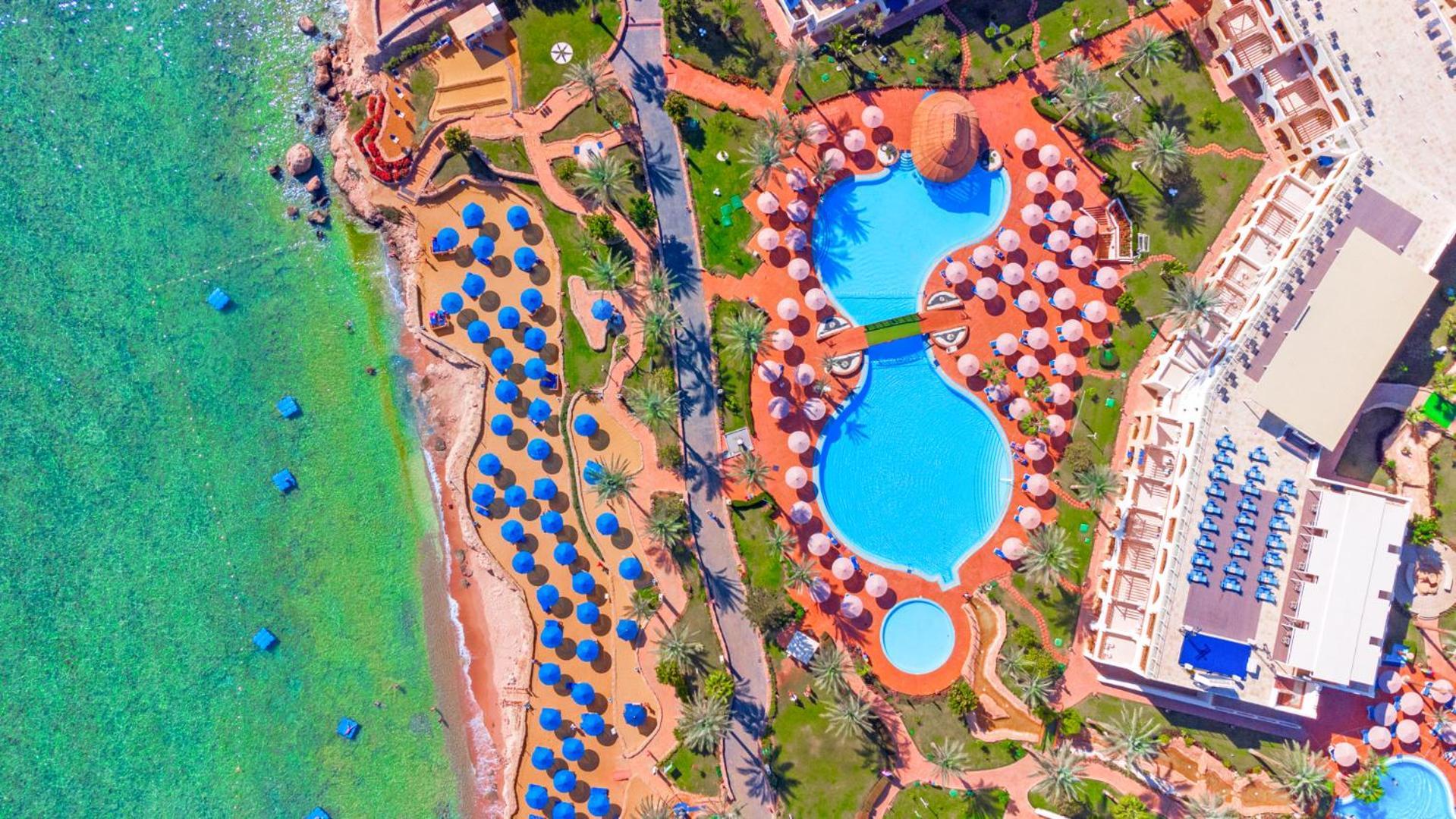 Pickalbatros Royal Grand Sharm - Adults Friendly 16 Years Plus ภายนอก รูปภาพ The photo shows an aerial view of a beach resort. In the foreground, there's a large swimming pool shaped like a flowing river, surrounded by lounge chairs and umbrellas. The pool has a distinctive, organic design with curved edges. To the left, ther