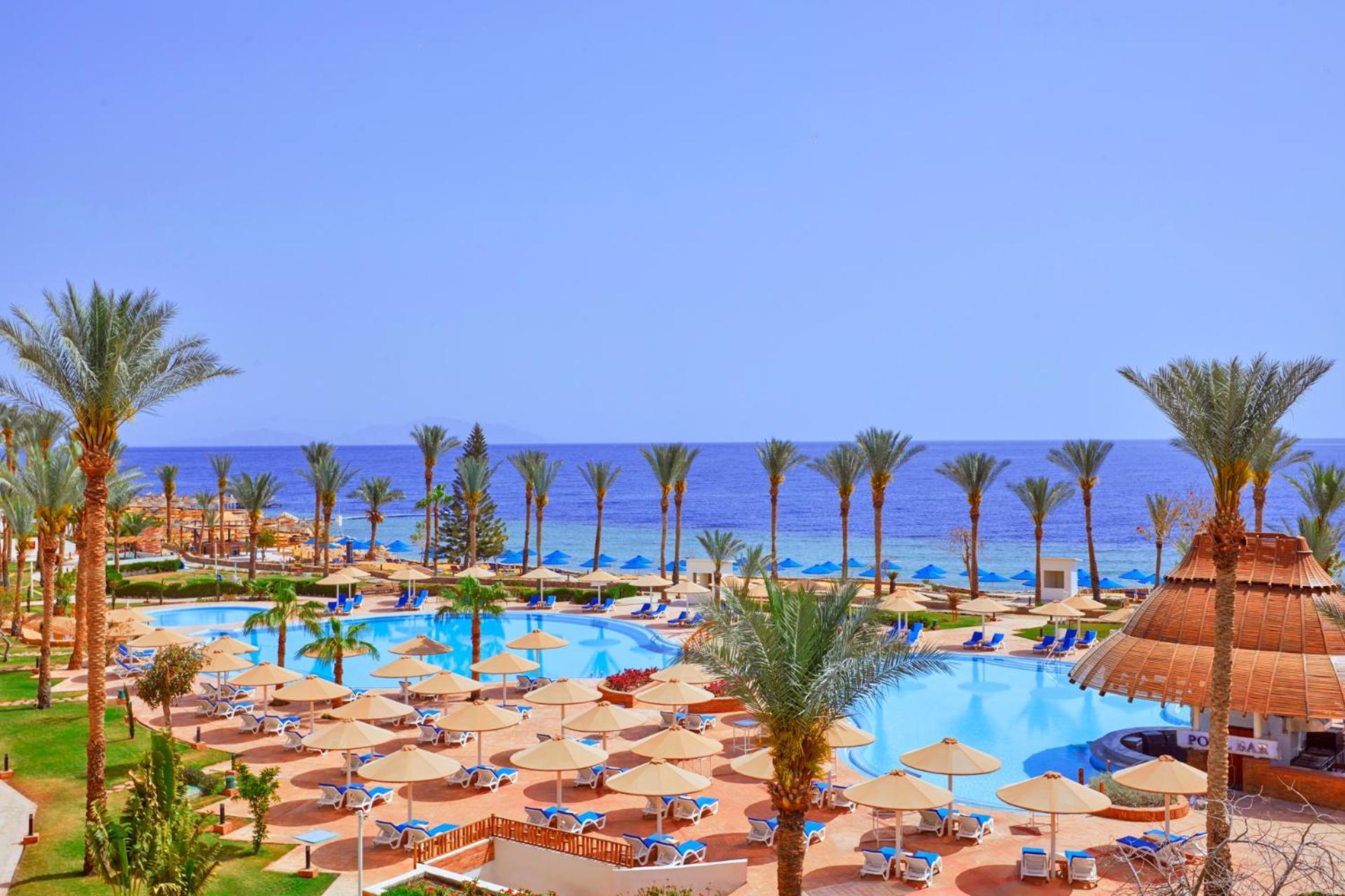 Pickalbatros Royal Grand Sharm - Adults Friendly 16 Years Plus ภายนอก รูปภาพ The photo showcases a beautiful resort setting by the sea. It features a large swimming pool surrounded by sunny lounge chairs and umbrellas, perfect for relaxation. The area is adorned with lush palm trees, adding to the tropical vibe. In the backgr