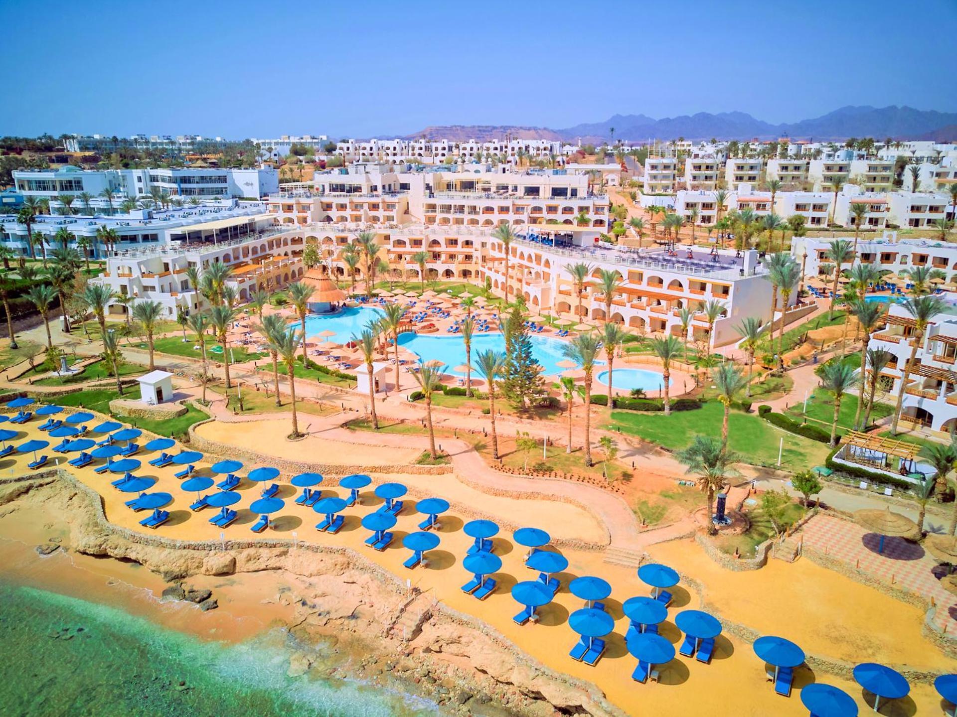 Pickalbatros Royal Grand Sharm - Adults Friendly 16 Years Plus ภายนอก รูปภาพ The photo shows a vibrant resort area with several buildings that appear to be accommodations or hotel units. There are multiple swimming pools surrounded by palm trees, creating a tropical atmosphere. In the foreground, there is a beach area with sa