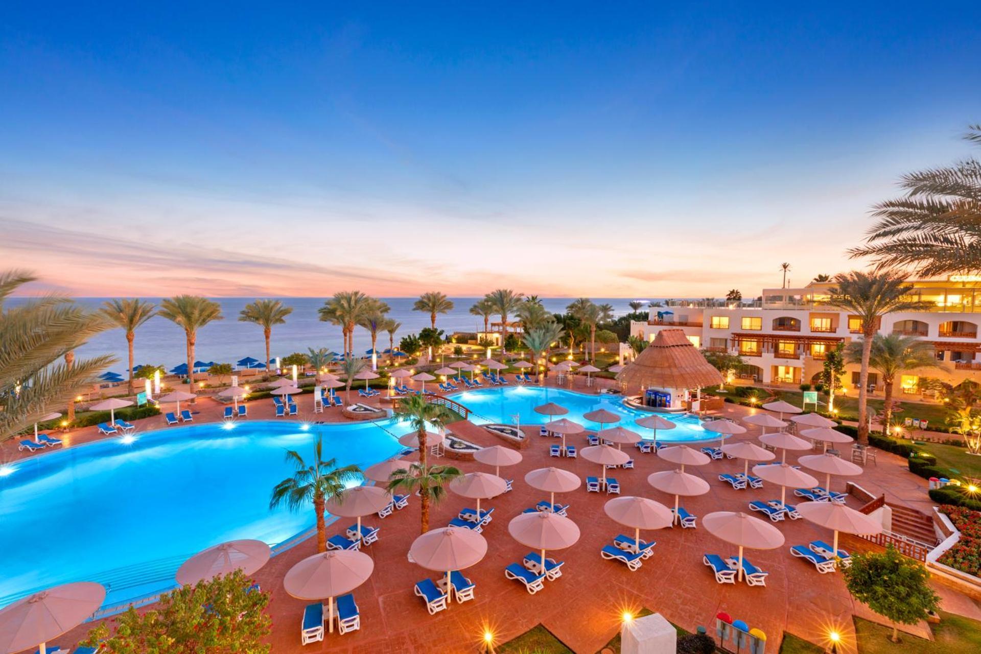 Pickalbatros Royal Grand Sharm - Adults Friendly 16 Years Plus ภายนอก รูปภาพ The photo showcases a luxurious resort setting with two large swimming pools, surrounded by lounge chairs and umbrellas. Palm trees are interspersed around the pool area, enhancing the tropical feel. In the background, there’s a view of the ocean, an
