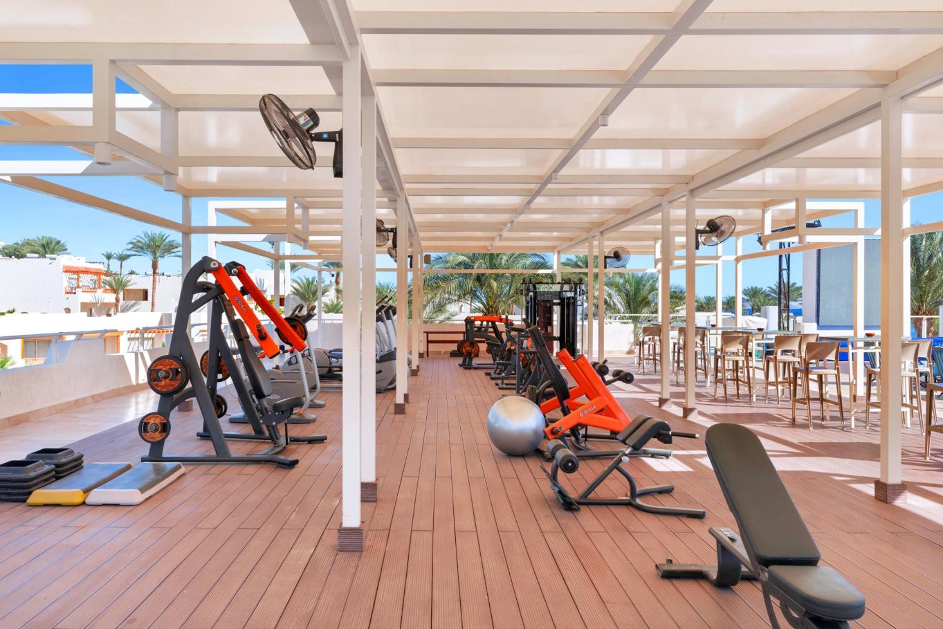 Pickalbatros Royal Grand Sharm - Adults Friendly 16 Years Plus ภายนอก รูปภาพ The photo depicts a gym area located outdoors or in a covered terrace, featuring various fitness equipment. There are several weight machines and benches, as well as some free weights. Large fans are installed for ventilation, and the space is design