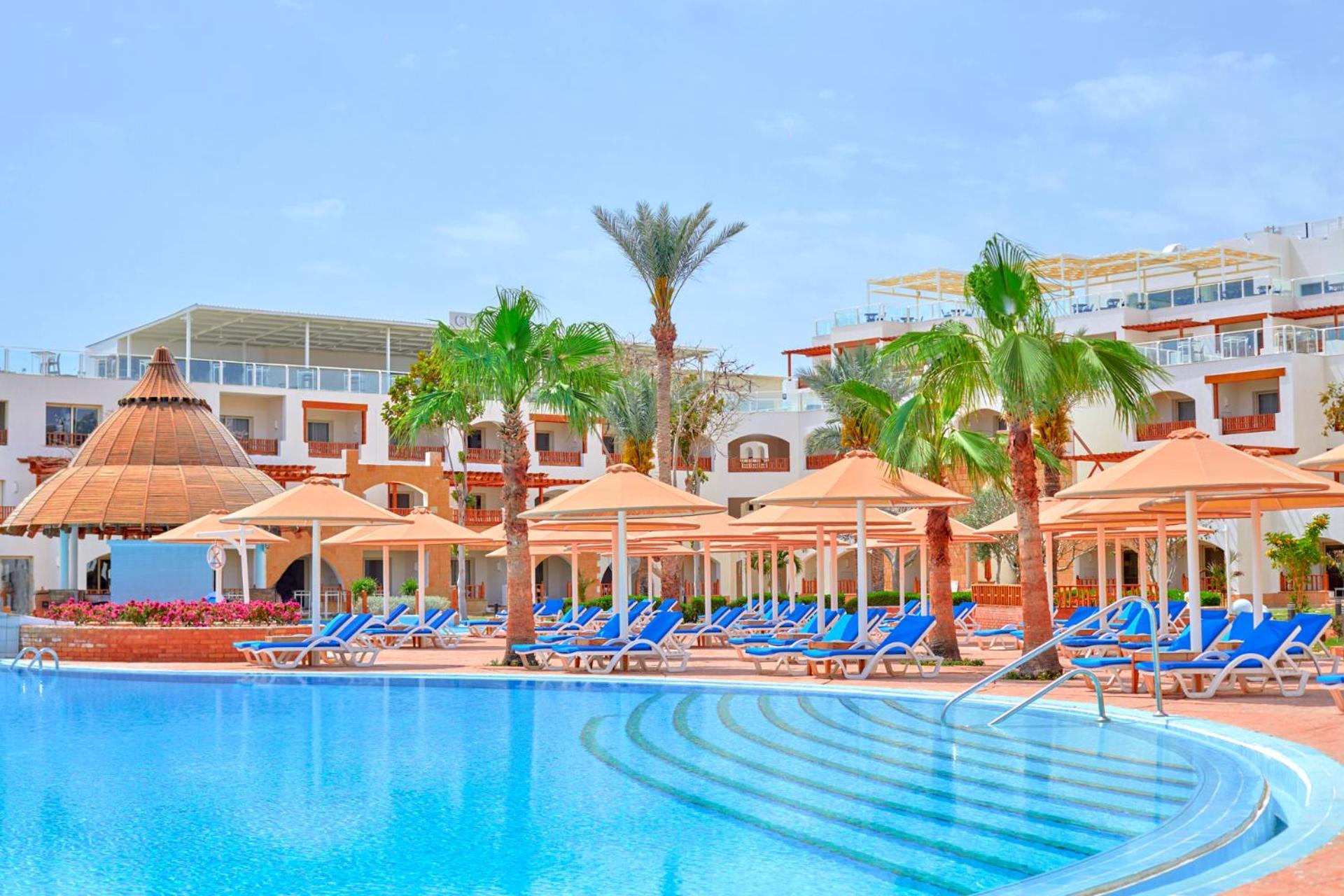 Pickalbatros Royal Grand Sharm - Adults Friendly 16 Years Plus ภายนอก รูปภาพ The photo depicts a resort scene featuring a beautiful swimming pool with clear blue water. Surrounding the pool are several lounge chairs arranged under large umbrellas, providing shade. In the background, there are palm trees that enhance the tropi