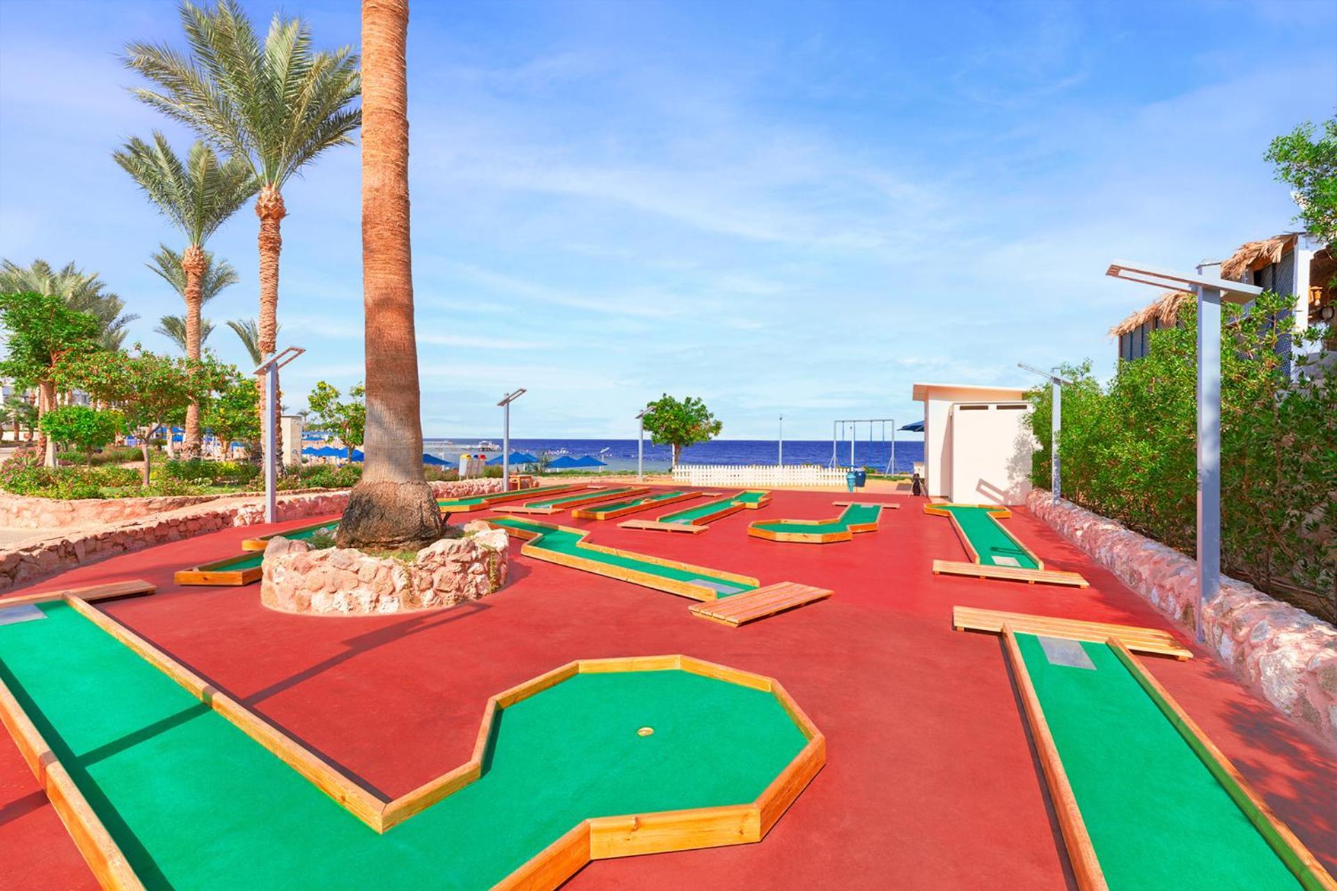 Pickalbatros Royal Grand Sharm - Adults Friendly 16 Years Plus ภายนอก รูปภาพ The photo shows a mini-golf course situated outdoors, with a view of the sea in the background. The course features vibrant green and red surfaces, laid out in winding patterns, and surrounded by well-maintained landscaping, including palm trees. The