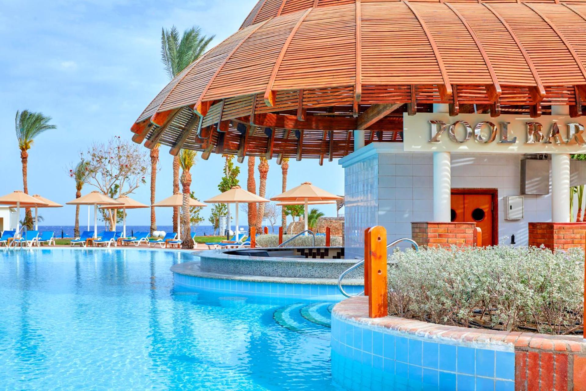 Pickalbatros Royal Grand Sharm - Adults Friendly 16 Years Plus ภายนอก รูปภาพ The photo depicts a picturesque pool area at a resort. In the foreground, there is a clear and inviting swimming pool with curved edges, surrounded by a light blue tile border. To the side, a pool bar is visible with a wooden roof and stylish archite
